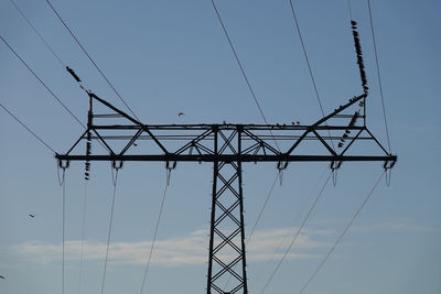 Low angle view of electricity pylon against blue sky