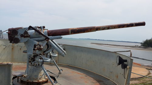 Close-up of rusty weapon by sea against sky