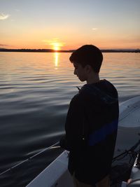 Man standing in sea against sky during sunset