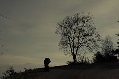 Silhouette man standing by bare tree against sky