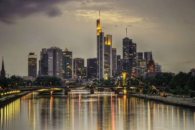 Illuminated buildings by river against sky in city