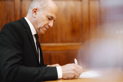 Side view of senior businessman signing contract document in board room