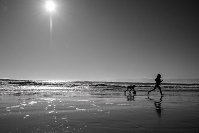 Silhouette children walking on beach against beach amd sky