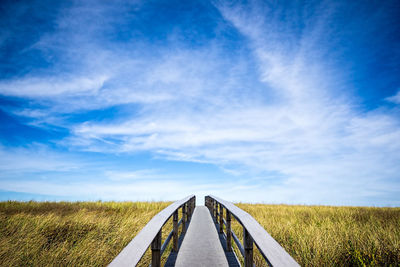 Footbridge over grassy field against sky