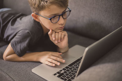 High angle view of boy using laptop while lying on sofa