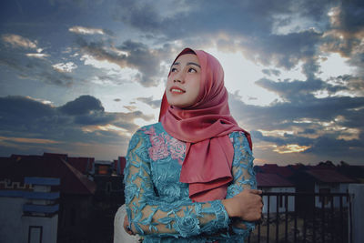 Smiling young woman in hijab standing against sky during sunset