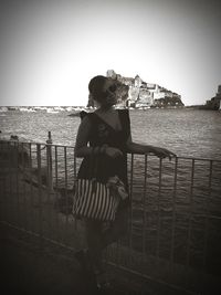 Woman standing by railing against sea against clear sky