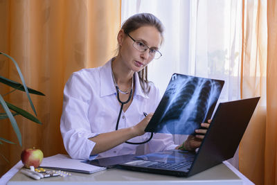 Portrait of female doctor holding x-ray while sitting at table