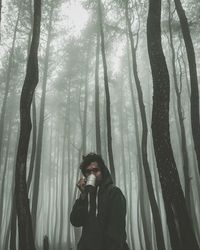 Man standing by tree trunk in forest