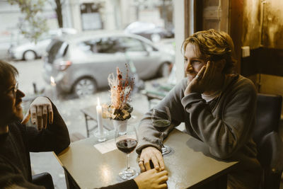 Smiling gay man leaning on elbow while talking with boyfriend sitting at restaurant