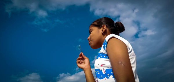 Low angle view of a girl standing against blue sky