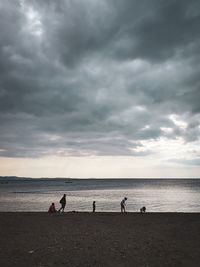 People at beach against storm clouds