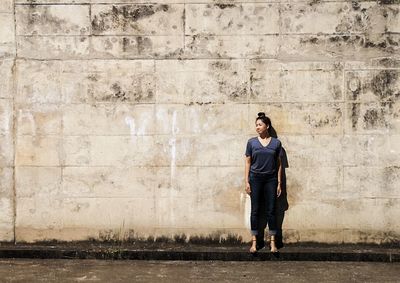 Full length of woman standing on footpath against wall