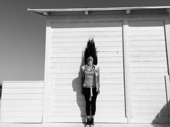 Woman standing with tousled hair against cottage on sunny day