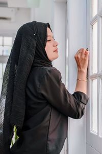 Portrait of young woman standing against window
