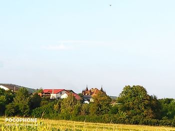 Houses and trees on field against sky