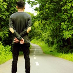 Rear view of man standing on road amidst trees