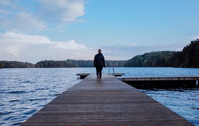 Man standing on pier over lake against sky