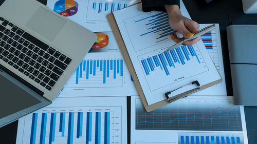 Cropped hand of businesswoman holding pen over graph and charts