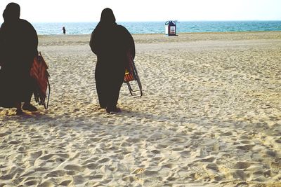 Rear view of men on beach against clear sky