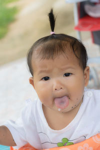 Portrait of cute baby girl sticking out tongue on stroller