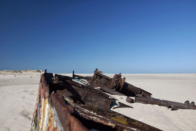 Abandoned boat on beach against clear blue sky