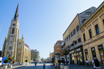 People on street amidst buildings against clear sky