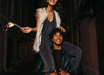 Portrait of smiling teenage boy carrying friend on shoulders at night