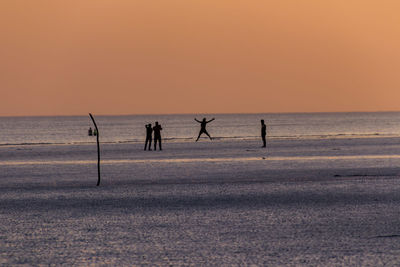 Silhouette people on beach against clear sky during sunset