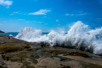 Waves splashing on shore against blue sky