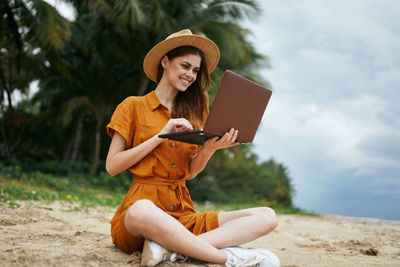 Full length of young woman using phone while sitting on land