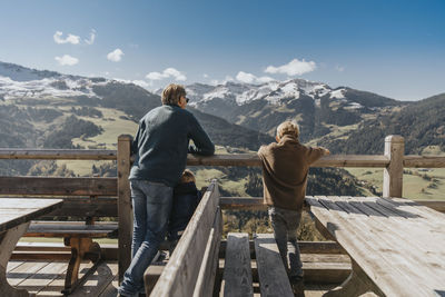 Father with two children leaning on railing while looking at leogang mountains, salzburger land, austria