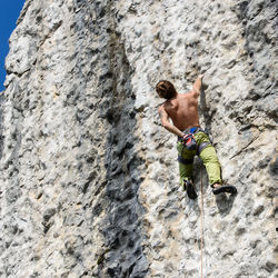 Rear view of shirtless man climbing on rock