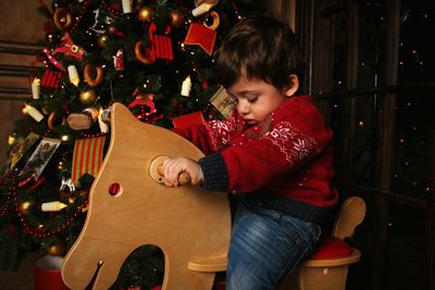 Boy riding on rocking horse by christmas tree at home