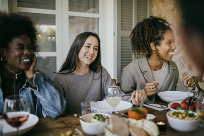 Happy female friends sitting together at dining table enjoying dinner in patio