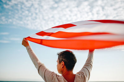 Rear view of man holding american flag against sky