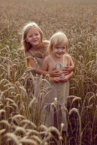 Two sisters blonde girls in dresses stand in a field with wheat ears in the summer