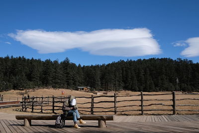 Rear view of woman sitting by railing against sky