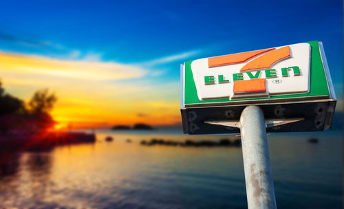 Information sign by sea against sky during sunset