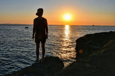 Rear view of man standing on beach during sunset