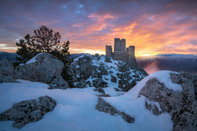 Snow covered buildings against sky during sunset