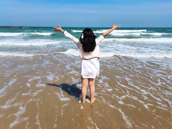 Rear view of woman with arms outstretched standing at beach