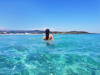 Rear view of woman swimming in sea against sky during sunny day