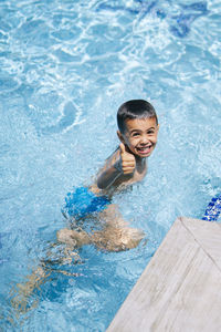 From above of happy boy swimming in clear sea water on sunny day and looking at camera with thumb up while enjoying summer vacation