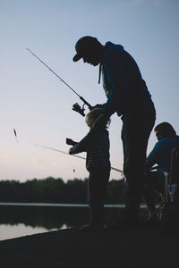 Side view of man fishing in lake against sky