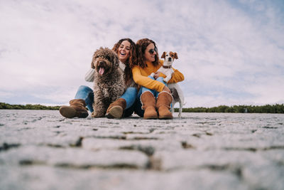 Female friends with dogs sitting on footpath