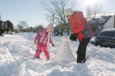 Grandmother and granddaughter building snowman in front yard