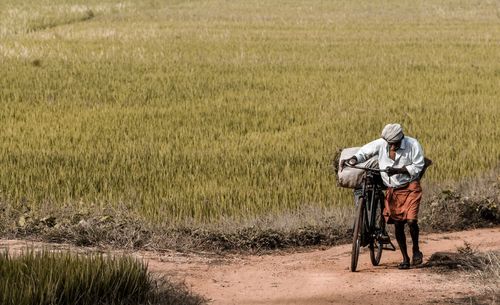 Man pushing bicycle on dirt road by arm