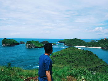 Rear view of man looking at sea against sky during sunny day