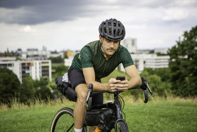 Man using mobile phone while sitting on bicycle on grassy land